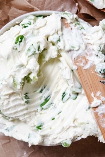 Bagel with scallion cream cheese spread and a knife.