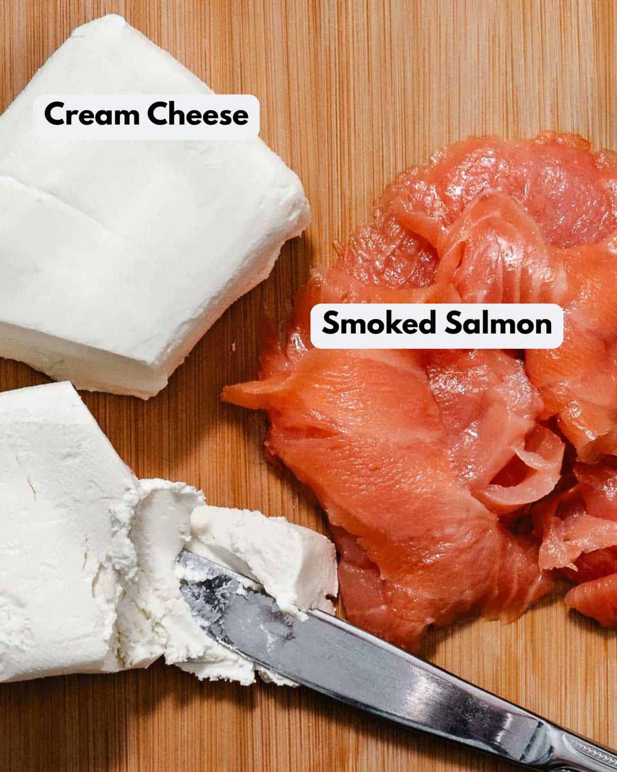 Blocks of cream cheese and smoked salmon on a cutting board with a butter knife.