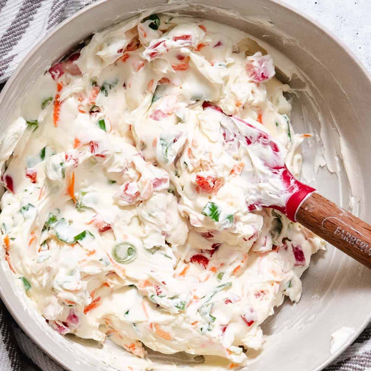 Vegetable cream cheese mixed with chopped scallions, carrot, red bell pepper, and watermelon radishes in a bowl.