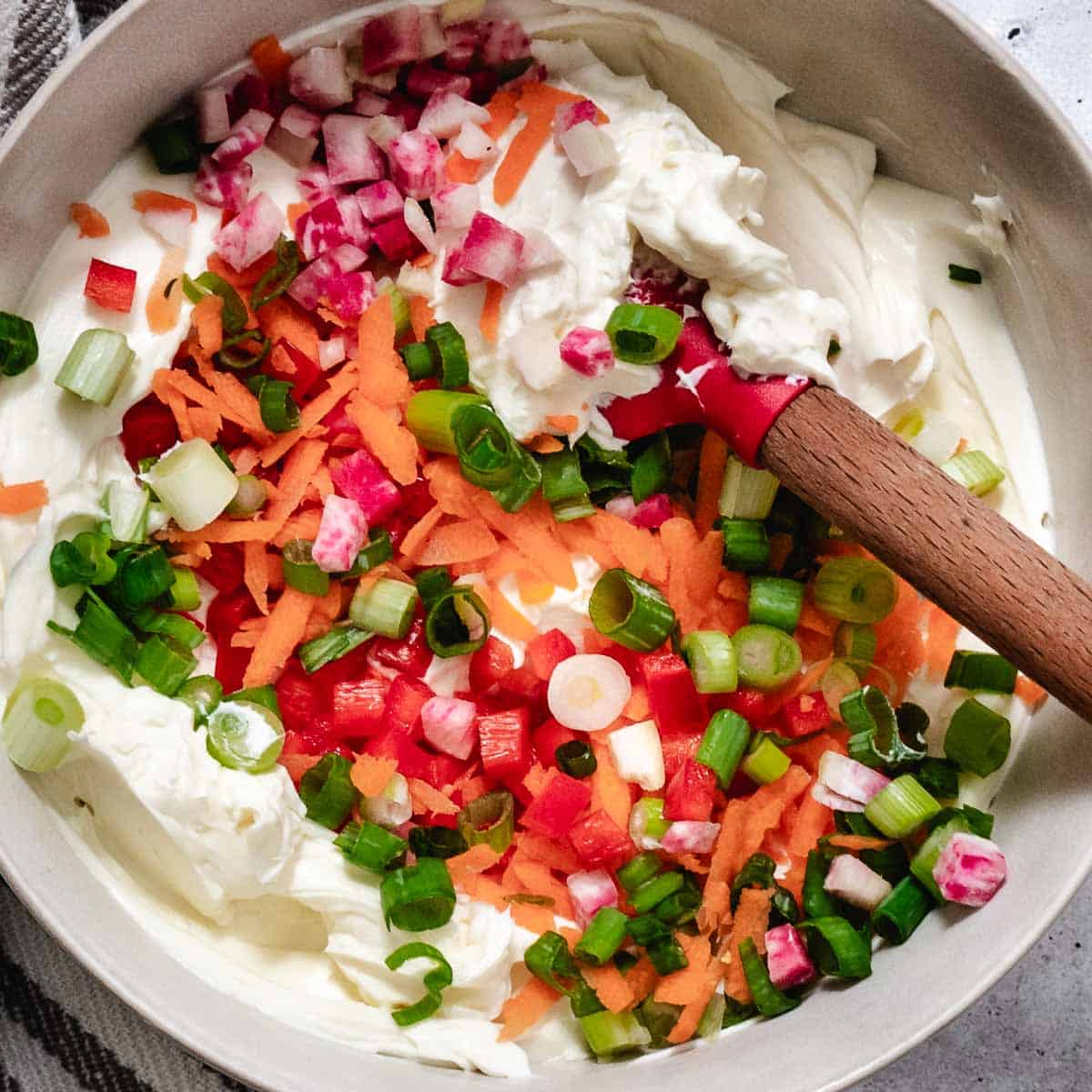 Veggie cream cheese mixed with scallions, carrot, red bell pepper, and watermelon radish in a bowl.