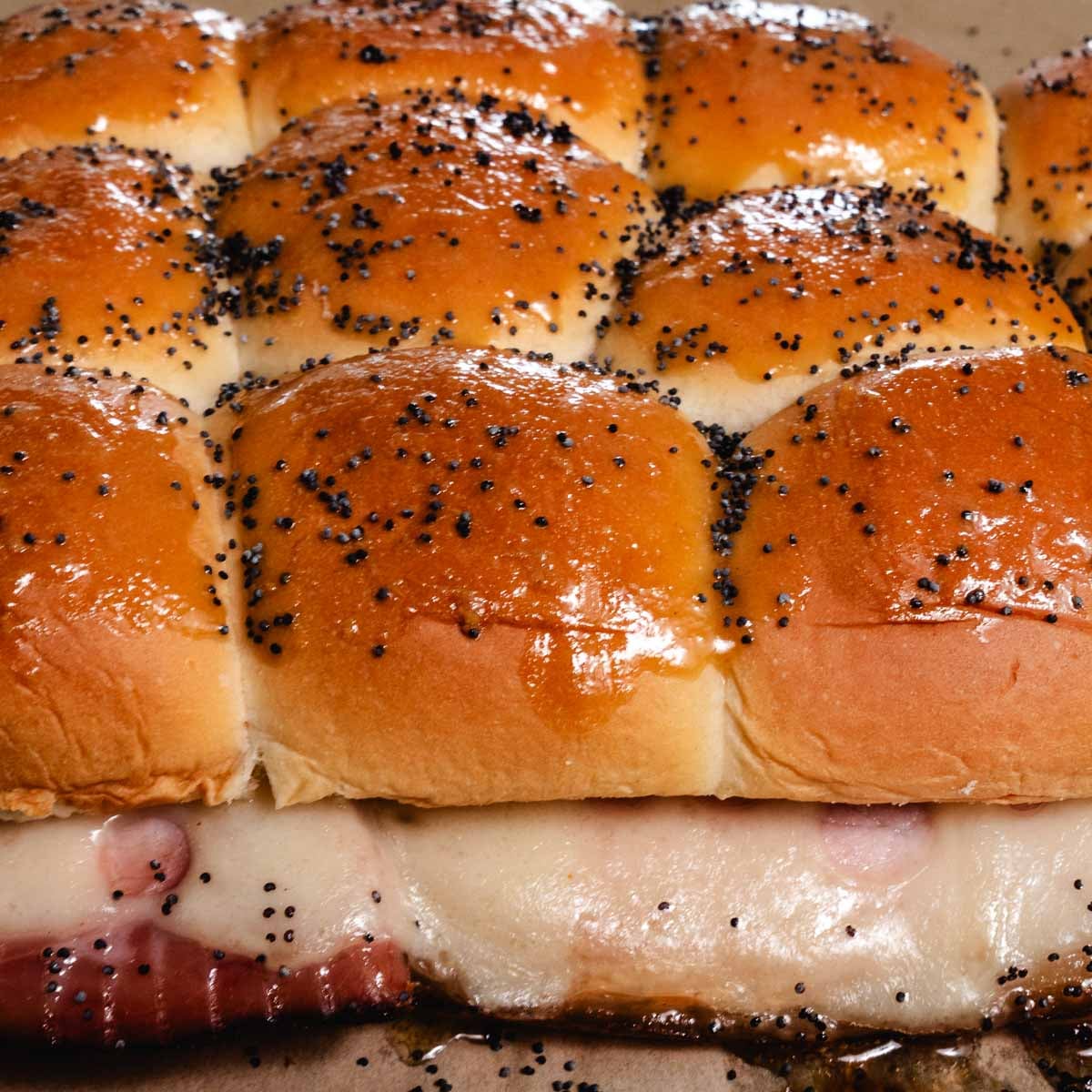 Ham and cheese sliders topped with butter and poppy seeds.