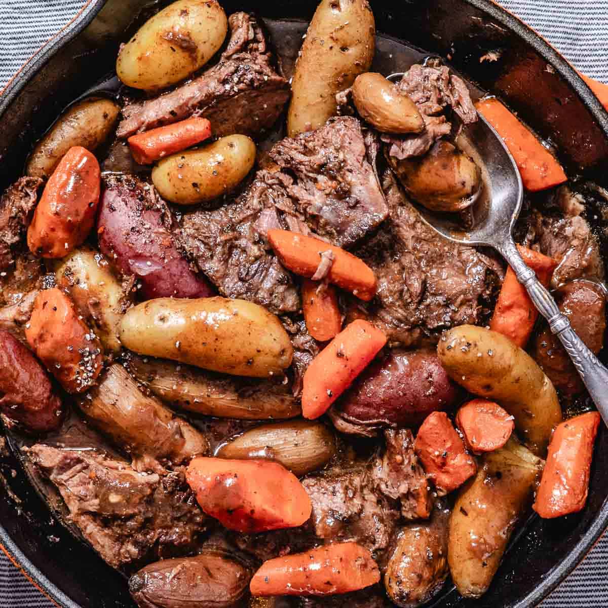Slow cooker pot roast with chunks of beef, potatoes, carrots, and onions in a rich brown cooking liquid.