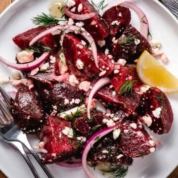 Beet salad with feta cheese, red onion, and fresh dill on a white plate with a lemon wedge and fork.