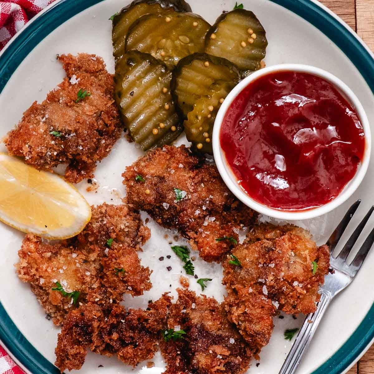Crispy fried chicken livers with parsley, sliced pickles, a lemon wedge, and red dipping sauce.