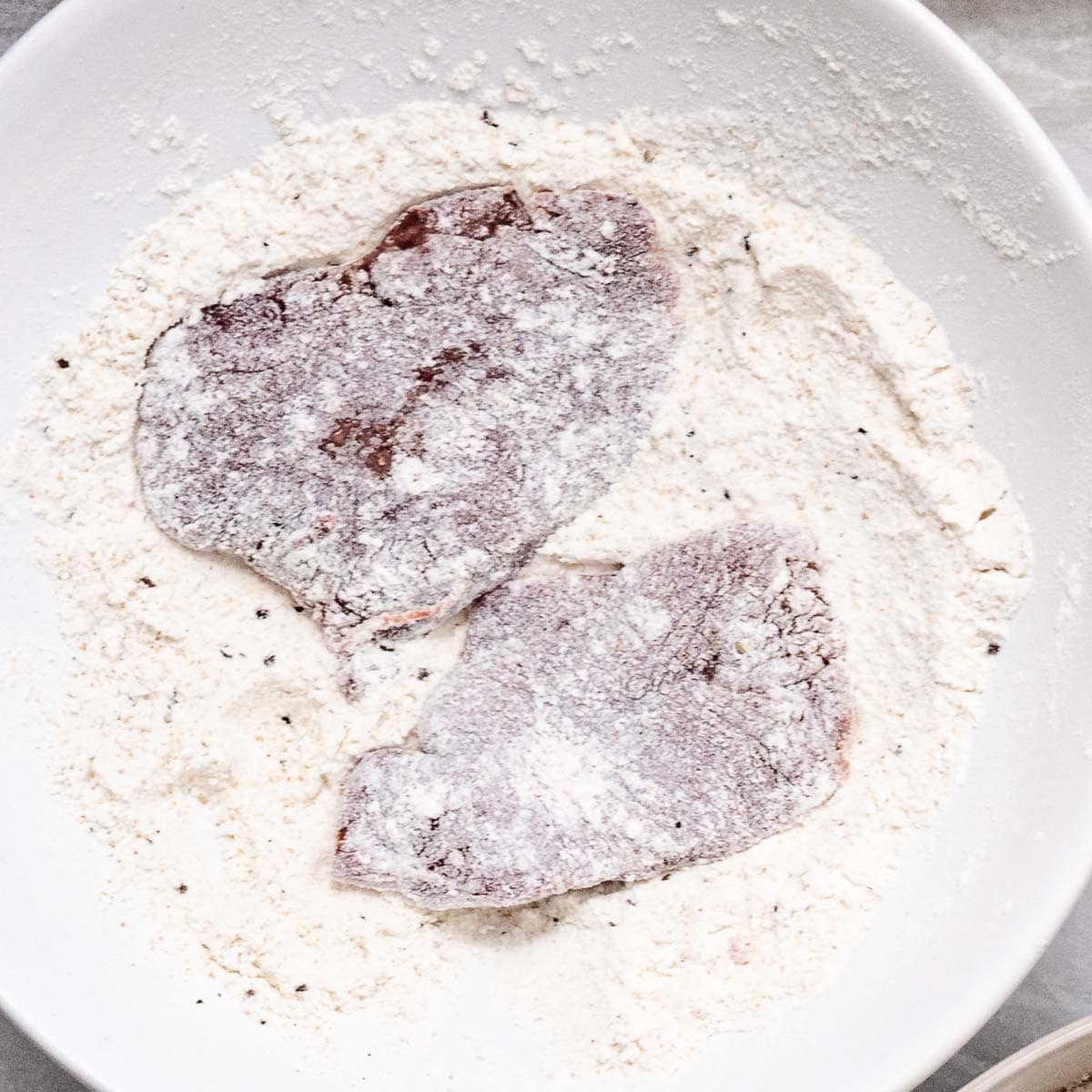 Chicken livers dredged in seasoned flour in a white bowl.
