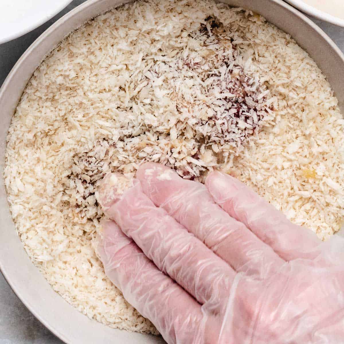 A gloved hand pressing chicken livers into panko breadcrumbs.