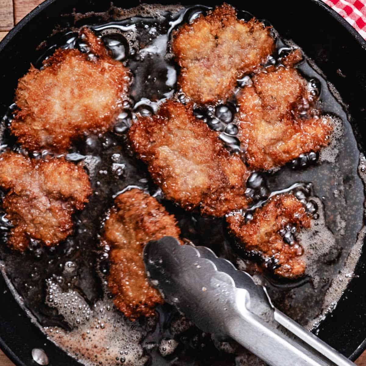 Panko-coated chicken livers frying in bubbling oil in a cast-iron skillet.