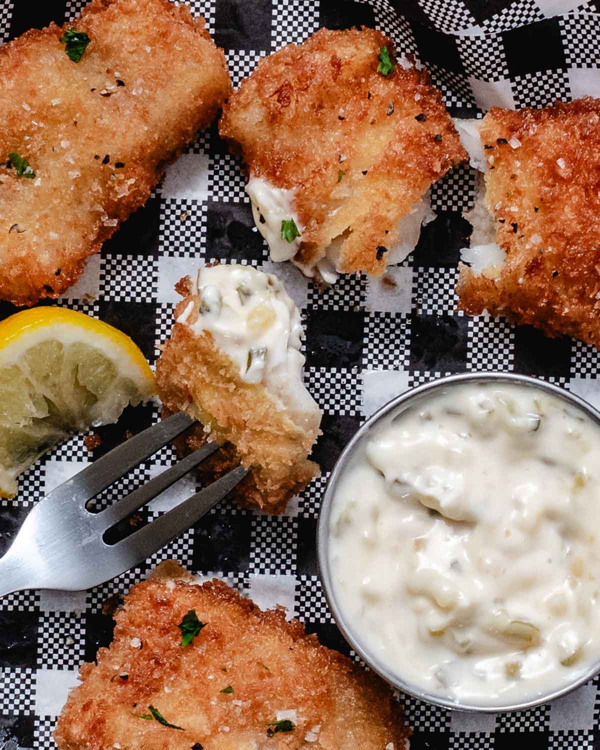 Golden panko-breaded pollock fillets served with a lemon wedge and a bowl of tartar sauce.