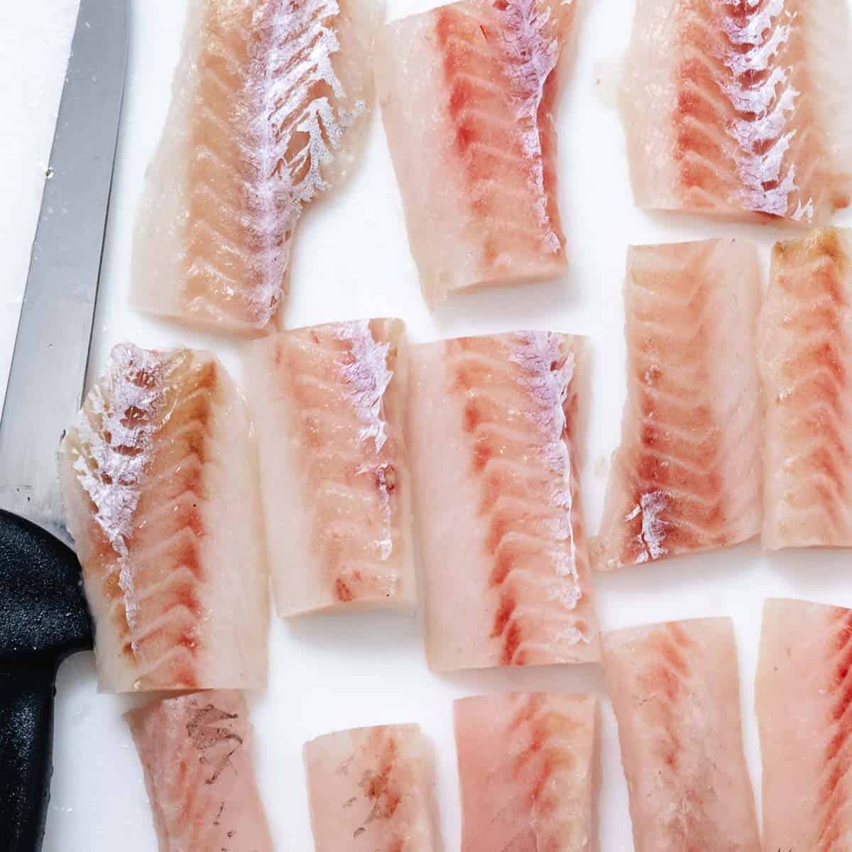 Raw pollock fillet pieces on a cutting board.