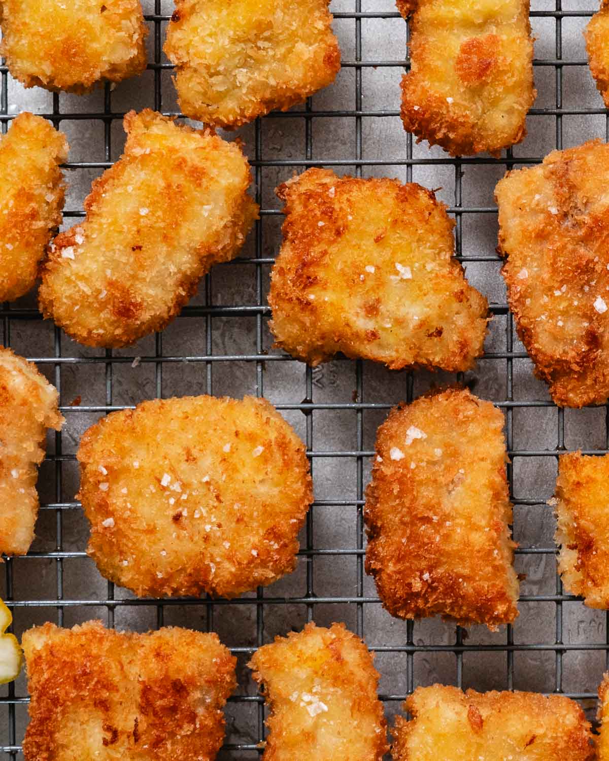 Golden, crispy fried pollock pieces sprinkled with flaky salt, cooling on a wire rack.