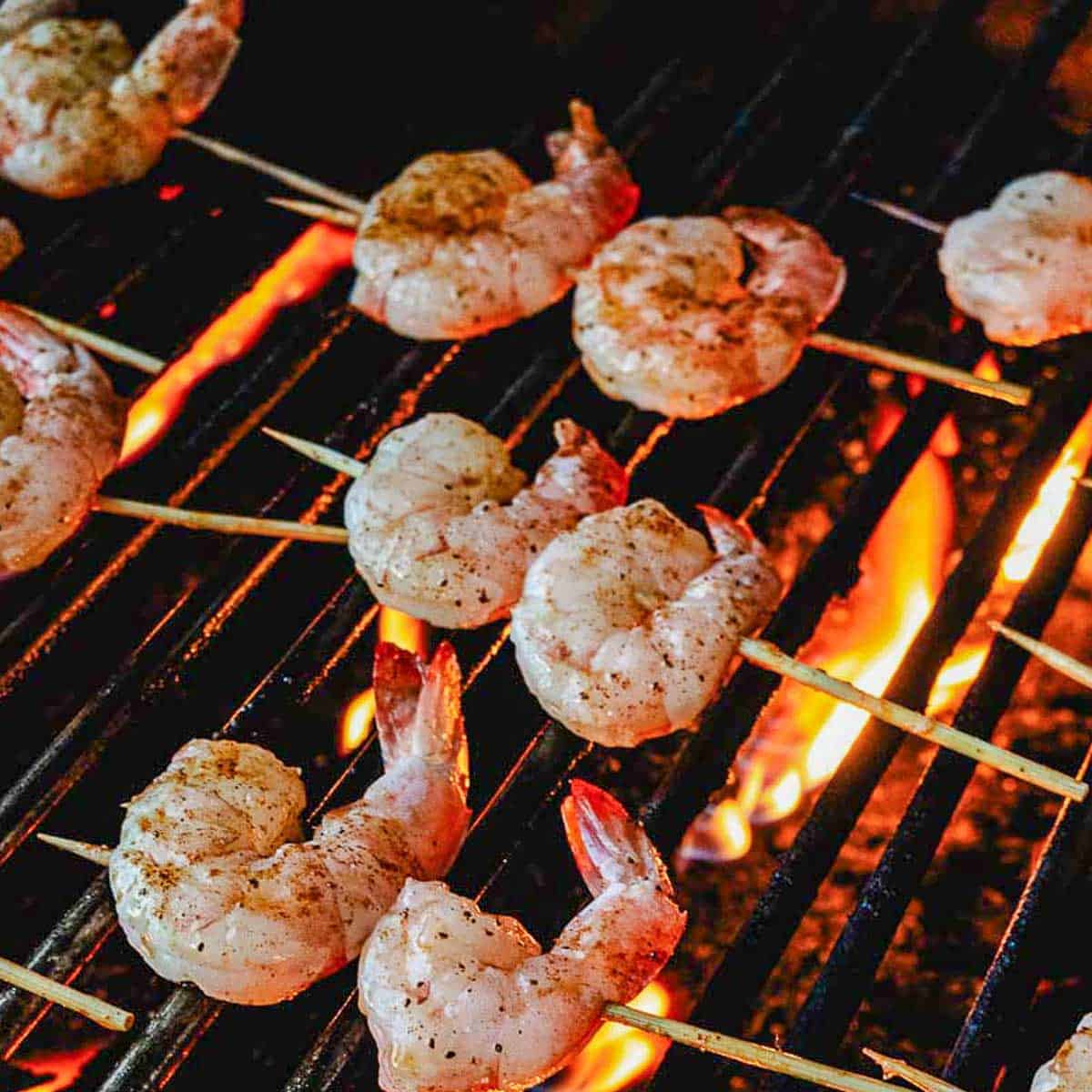 Mini shrimp skewers cooking on grill grates over an open flame.