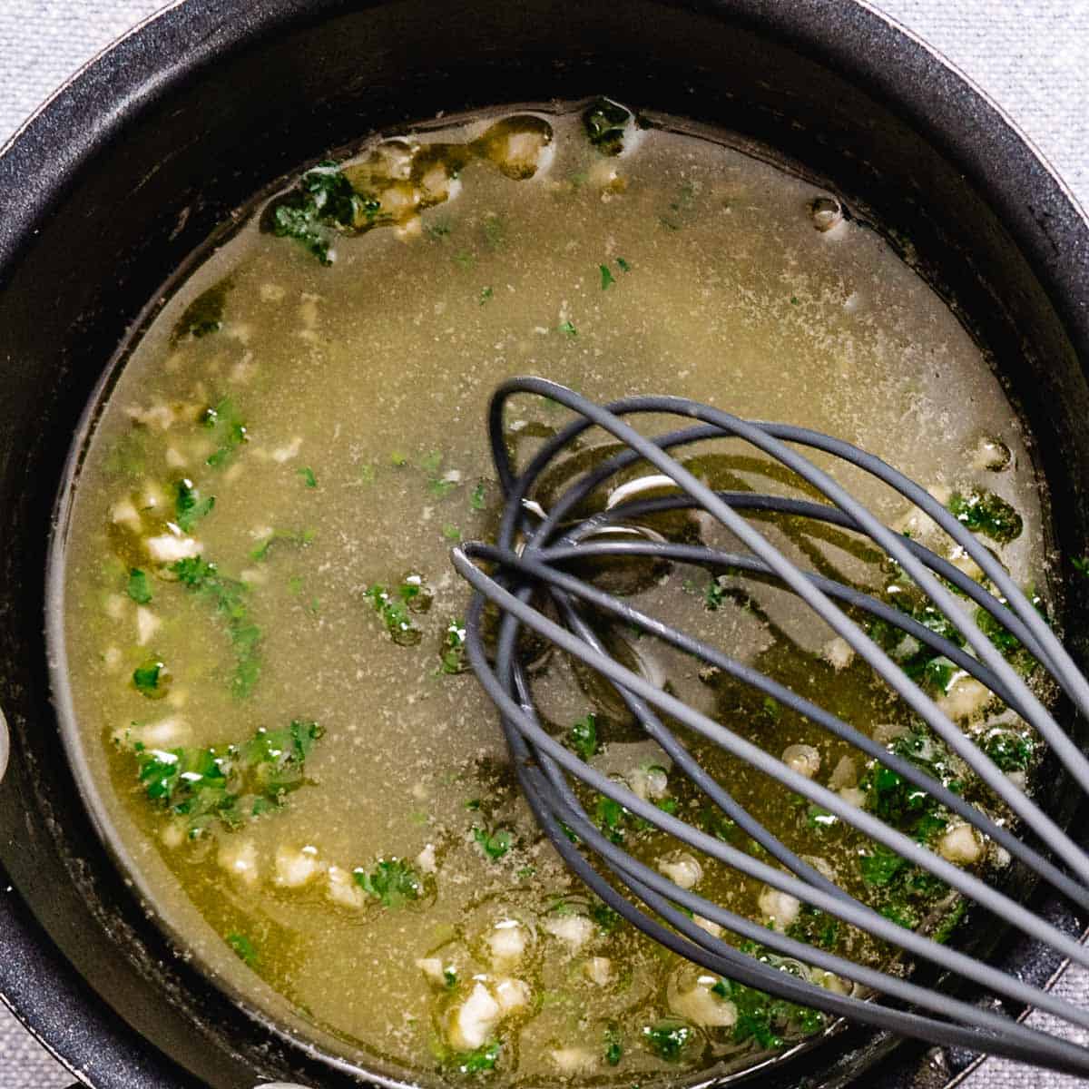 Whisking garlic butter sauce in a saucepan.