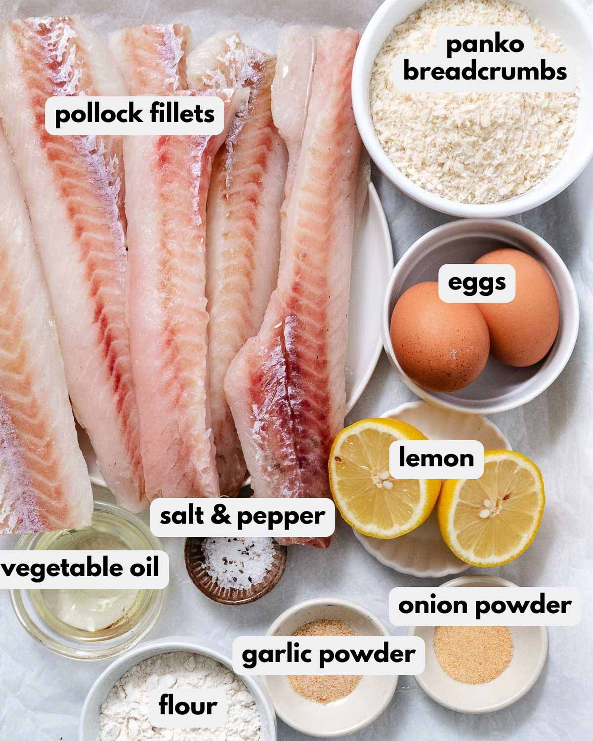 Ingredients for crispy fried pollock: raw pollock fillets, panko breadcrumbs, eggs, halved lemon, flour, vegetable oil, salt and pepper, garlic powder, and onion powder.