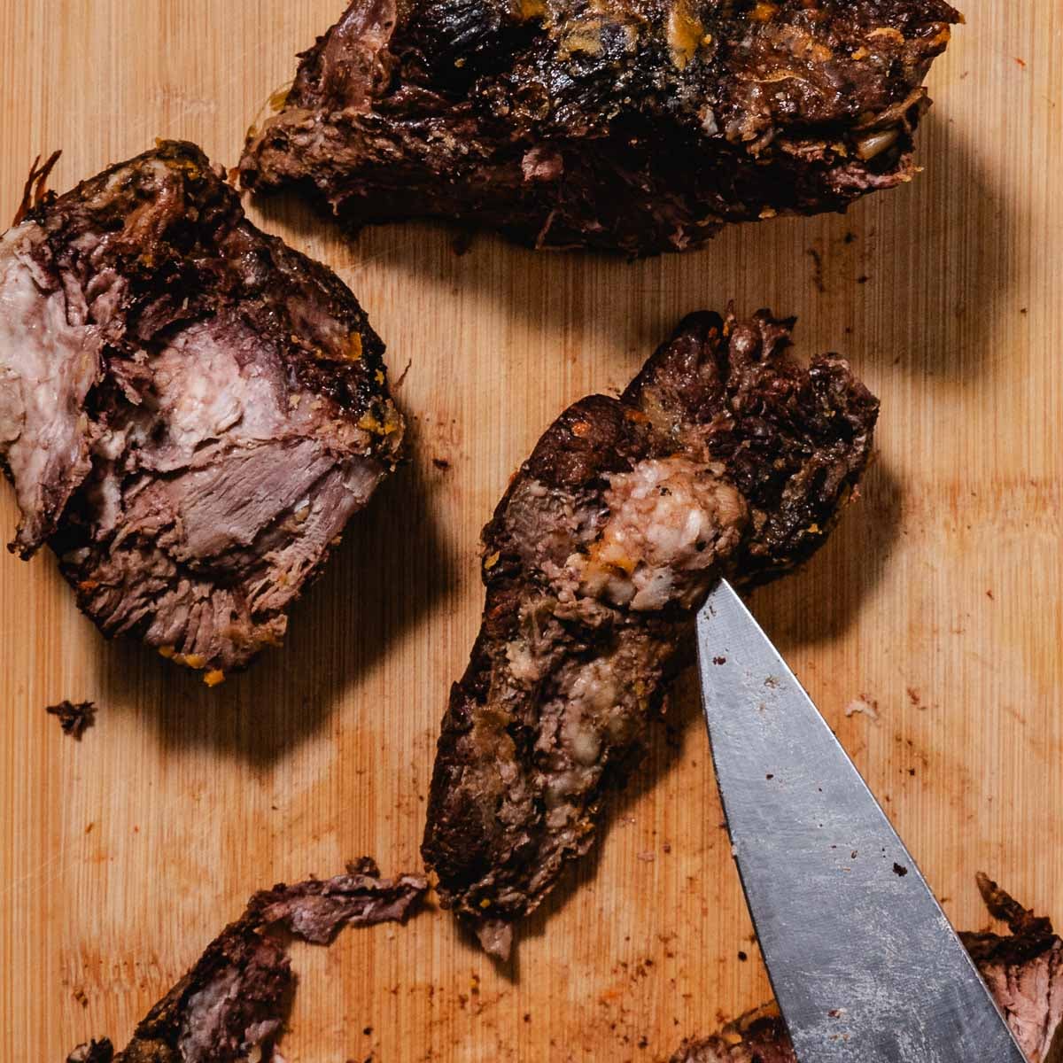 Knife trimming a pocket of fat from cooked chuck roast on a cutting board.