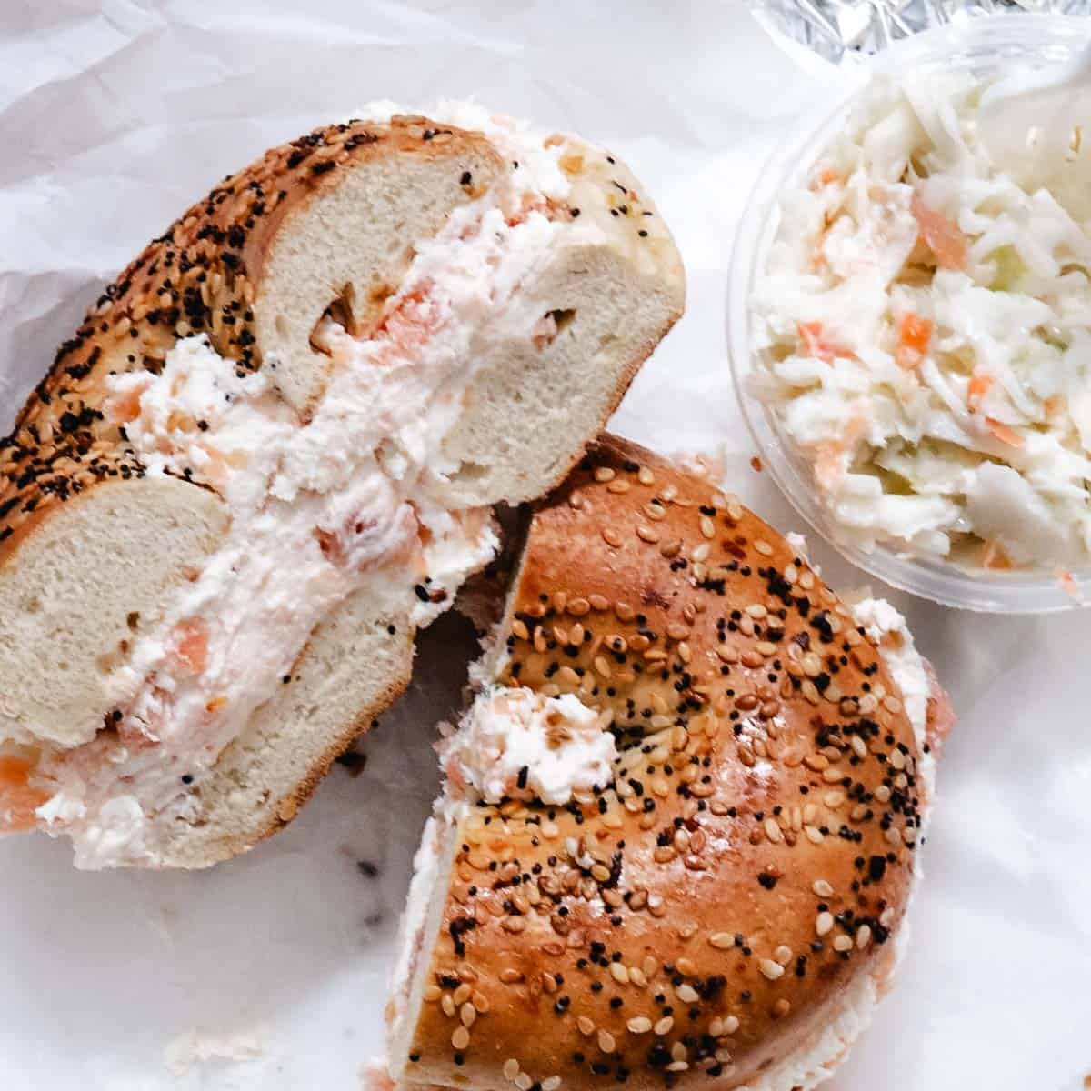 Smoked salmon cream cheese on everything bagel with a side of coleslaw.