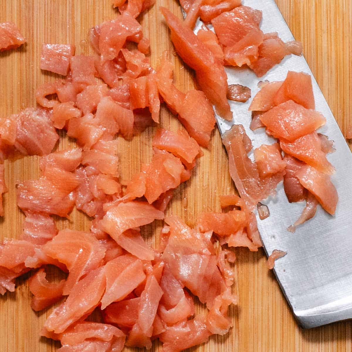 Chopped smoked salmon on a cutting board beside a chef's knife.