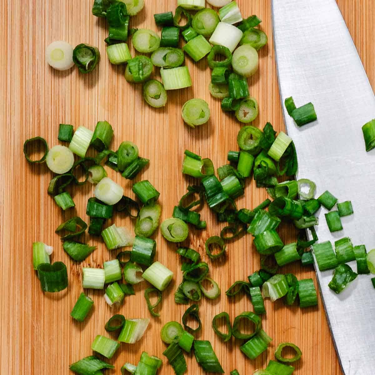 Chopping green onions, scallions, on a cutting board with chef's knife.