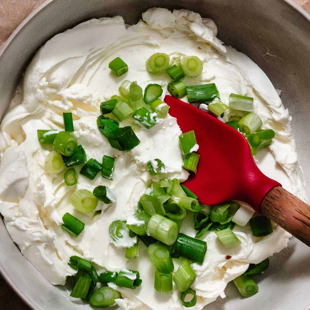 Mixing bowl with spring onions and cream cheese with a rubber spatula.