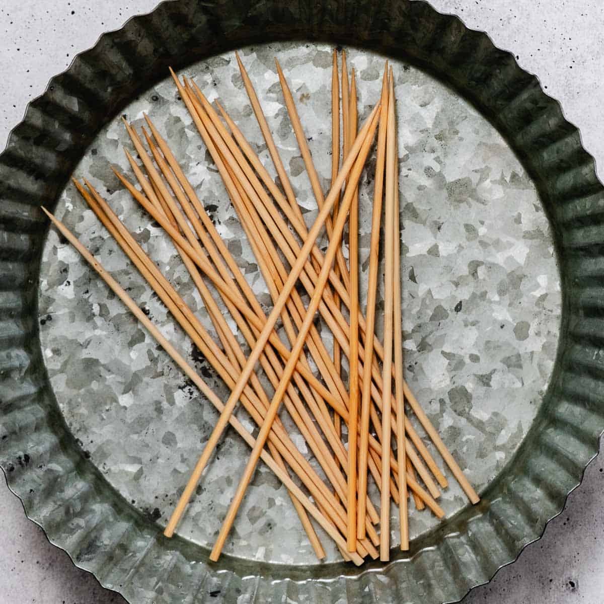 Short wooden skewers soaking in water in a shallow metal pan.