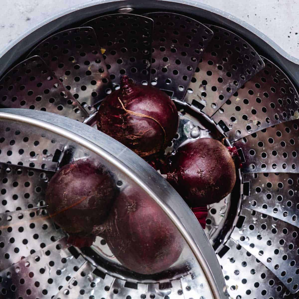Whole red beets in a steamer basket.